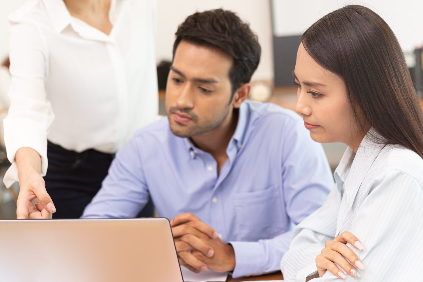An Asian business man and woman discuss a matter in front of an open laptop.