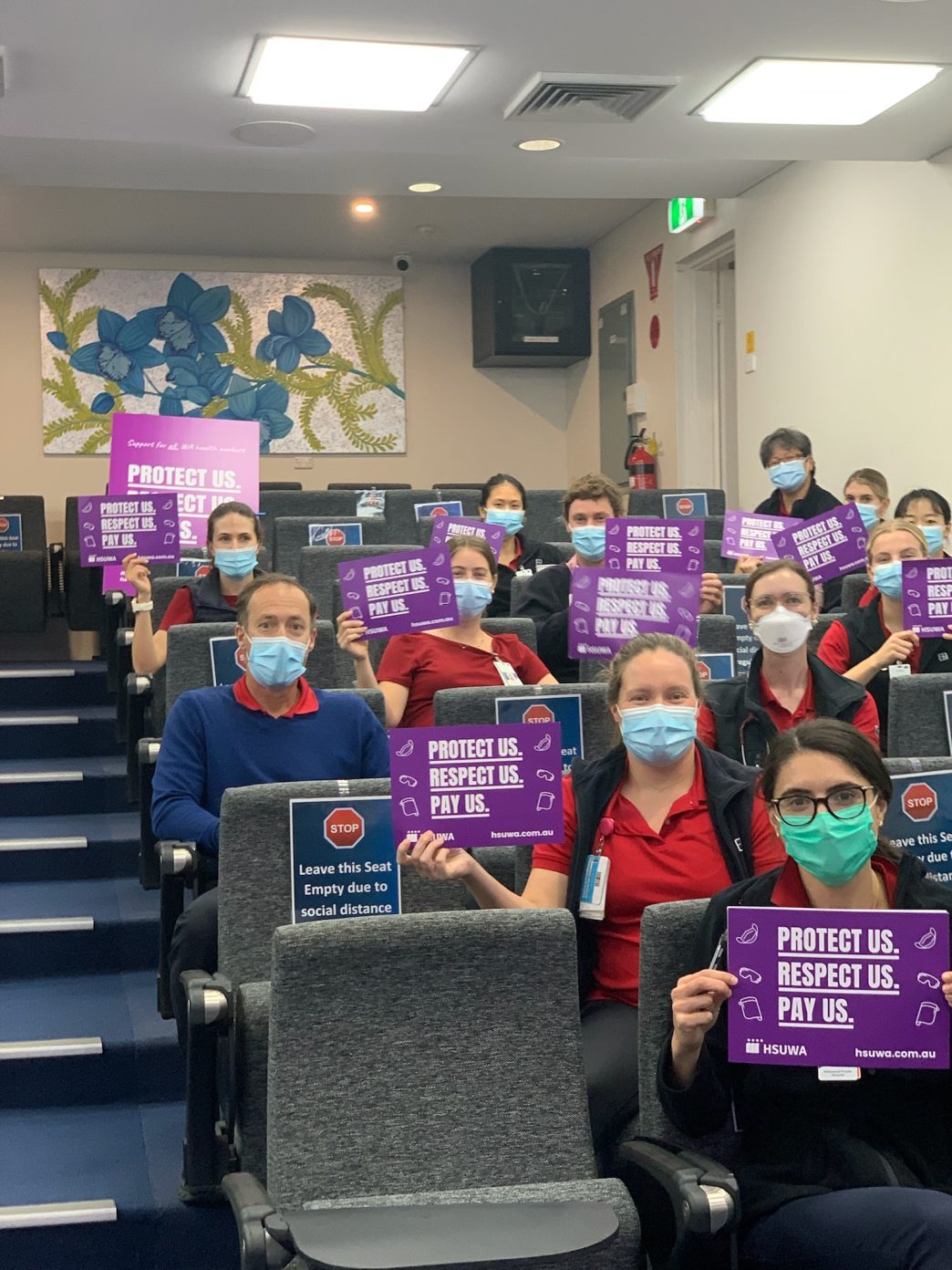 Members at Hollywood Private Hospital sit in a lecture theatre and hold up purple HSUWA signs.