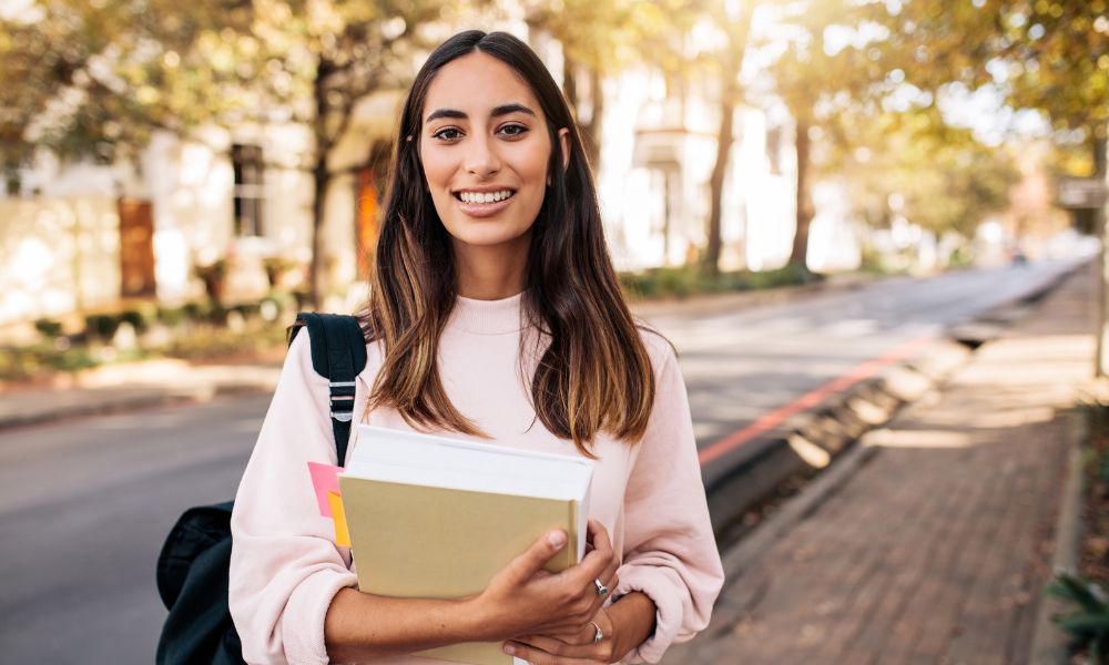 A health student smiles at the camera holding her text books.