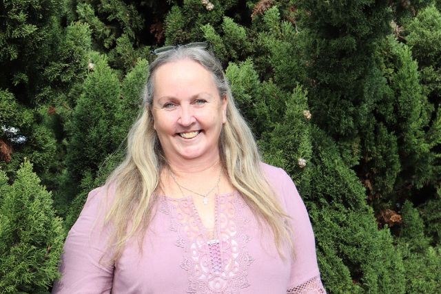 Delegate Bianka stands, smiling in front of green trees. She has long blonde hair and a pink shirt.
