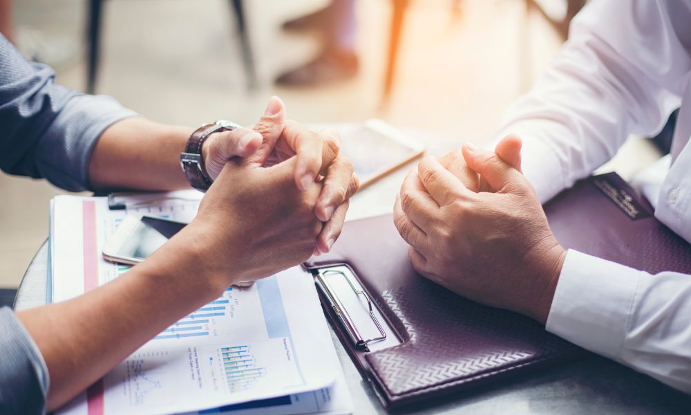 Two sets of hands sit at a bargaining table on top of files.