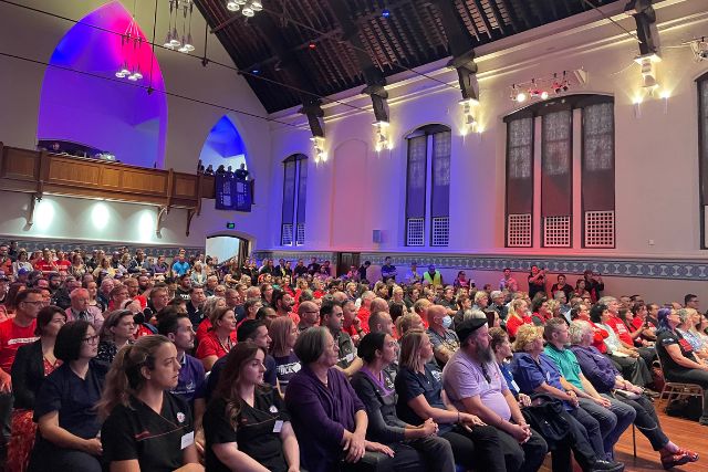 HSUWA Members sit in two rows at the front of a packed Public Sector Town Hall Meeting with other public sector workers.