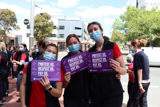 Three Allied Health professionals at Ramsay Health Care hold up Protect Us. Respect Us. Pay Us. signs.