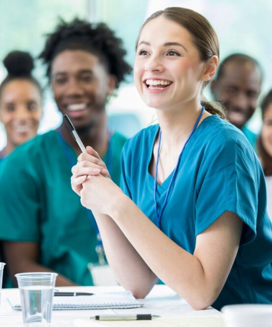 Group of health students in scrubs with a female health student holding a pen in the foreground.