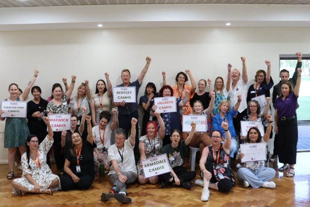 Members from CAMHS stand together holding signs with their left fists in their air at a Stop Work Meeting.