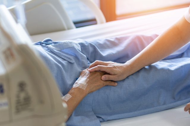 Close up of a health care worker holding a palliative care patient's hand.
