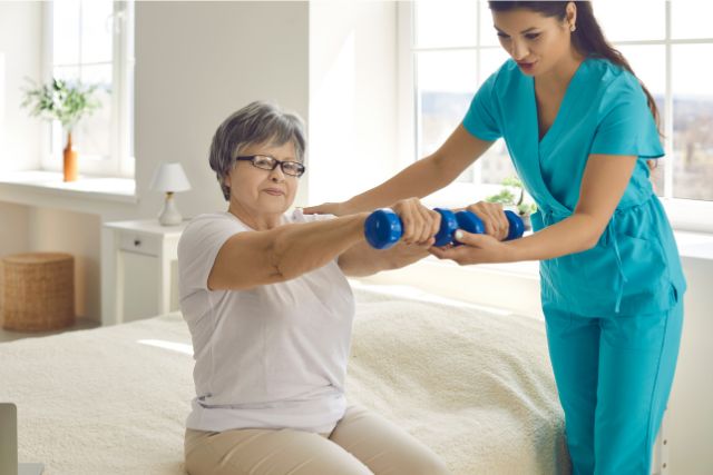 Elderly woman lifts small dumbells with her aged care physiotherapist.