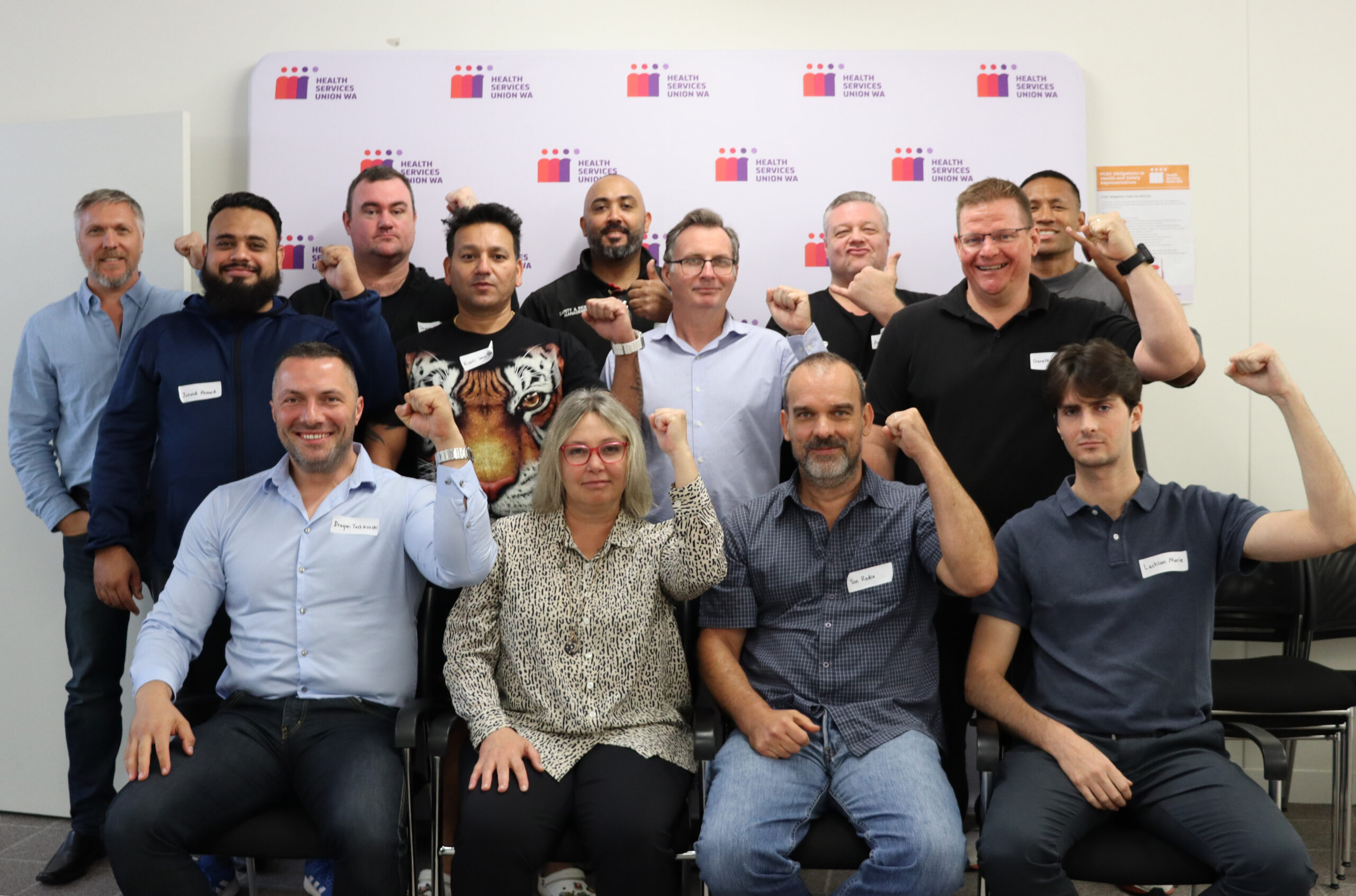 A group of Security Officers with fists raised, stand and sit with HSUWA Secretary Naomi McCrae.