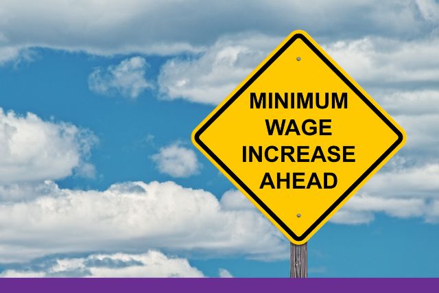 Blue sky with a yellow sign that states "Minimum wage increase ahead."